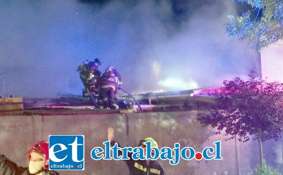 Personal de Bomberos trabajando sobre el techo para combatir el fuego.
